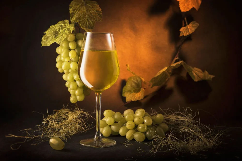 A sophisticated still life of a wine glass with green grapes and vine leaves on a warm, moody backdrop