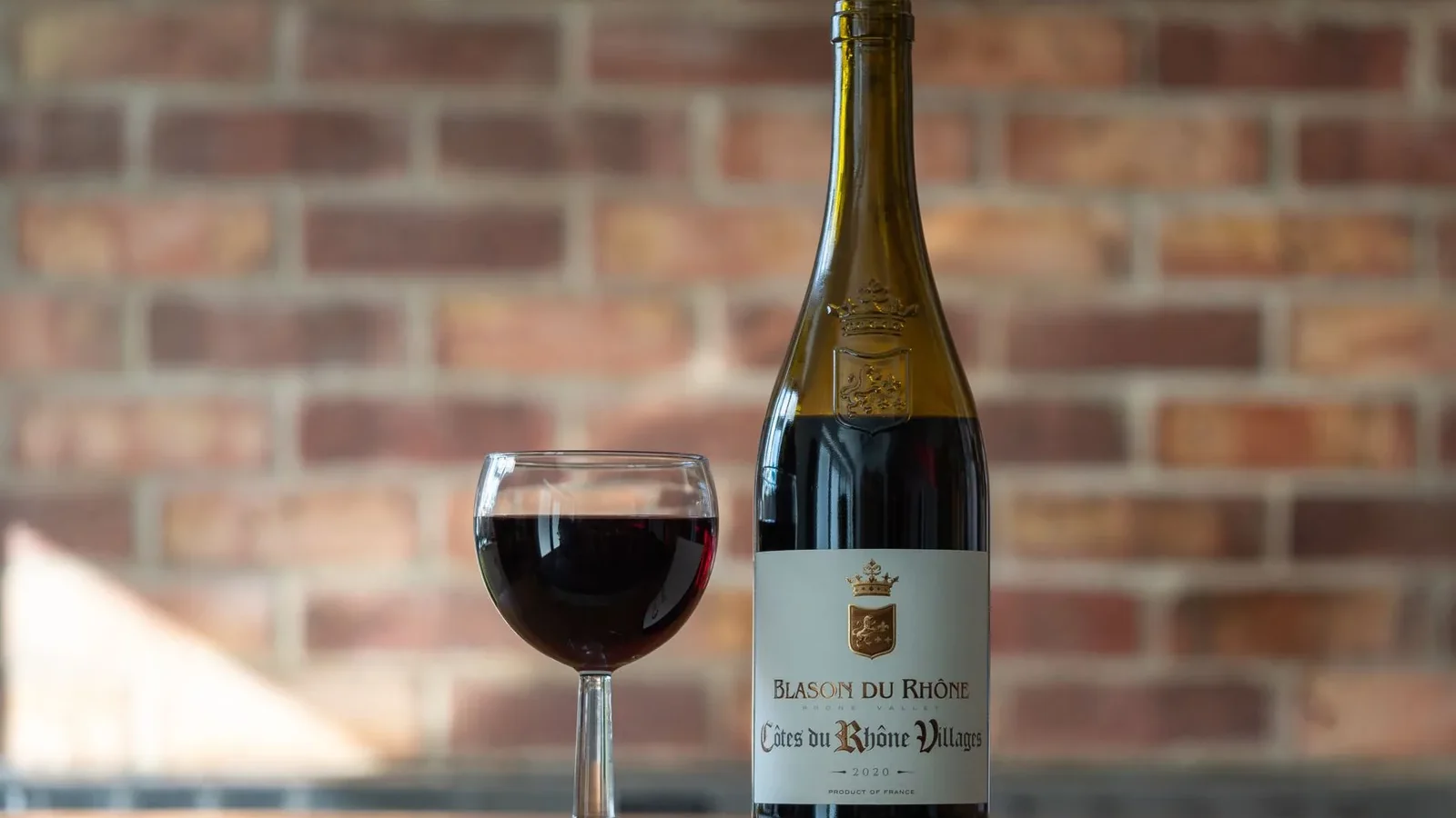 A sophisticated still life showcasing a bottle and glass of red wine against a brick background