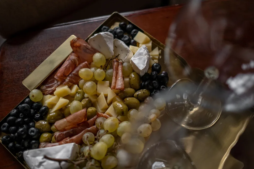 A stylish cheese and charcuterie board with olives, grapes, and a wine glass on a tray indoors
