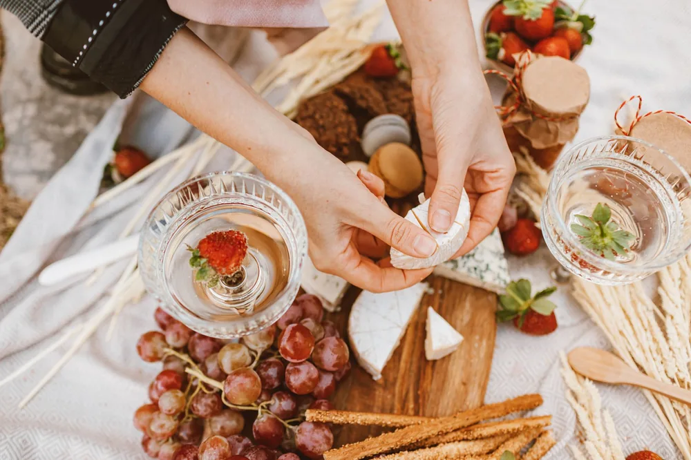 A stylish gourmet picnic display featuring cheese, grapes, and sparkling drinks adorned with strawberries
