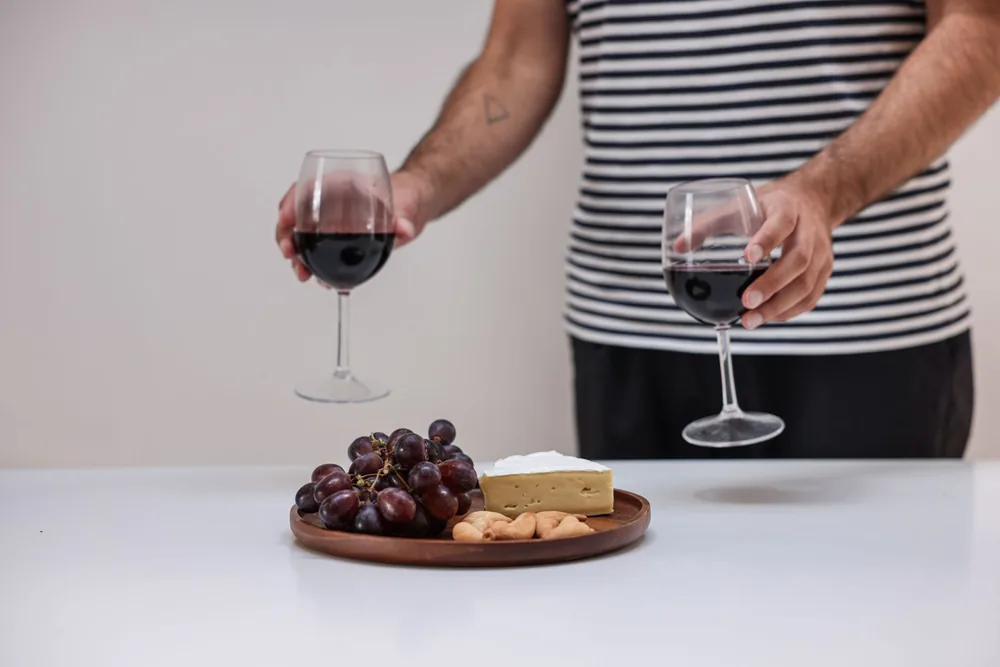 A stylish setup of red wine with cheese and grapes on a charcuterie board