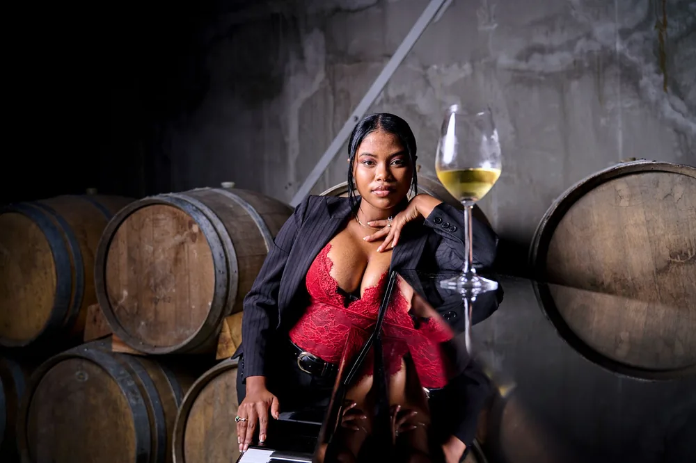 A stylish woman poses with a glass of wine in a rustic winery setting