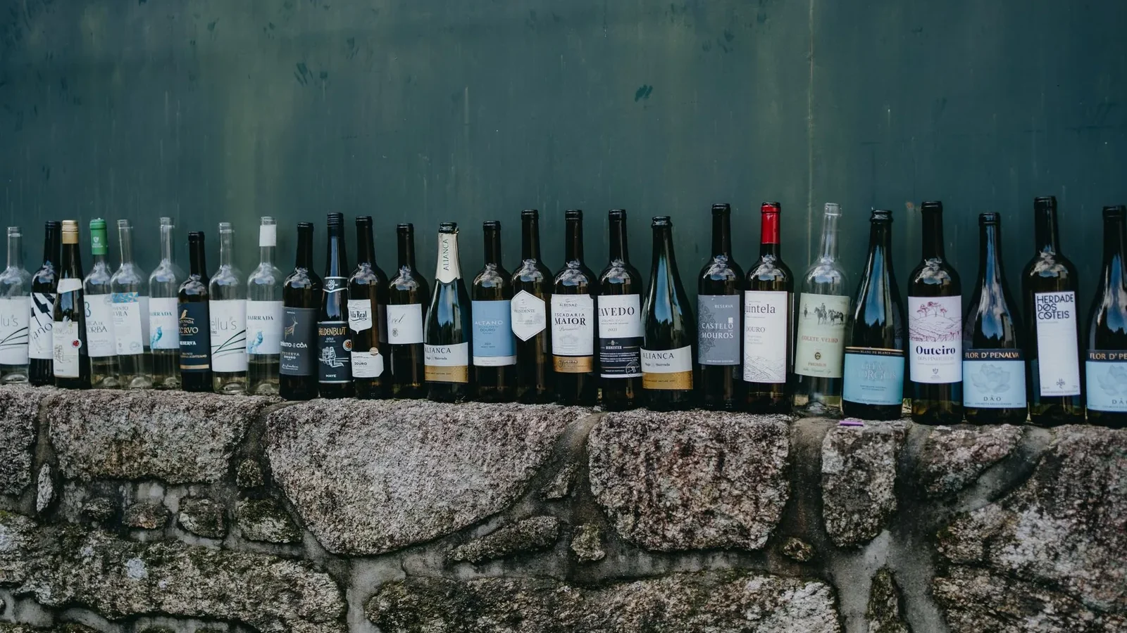 A variety of wine bottles displayed on a rustic stone wall, captured outdoors for a vintage feel
