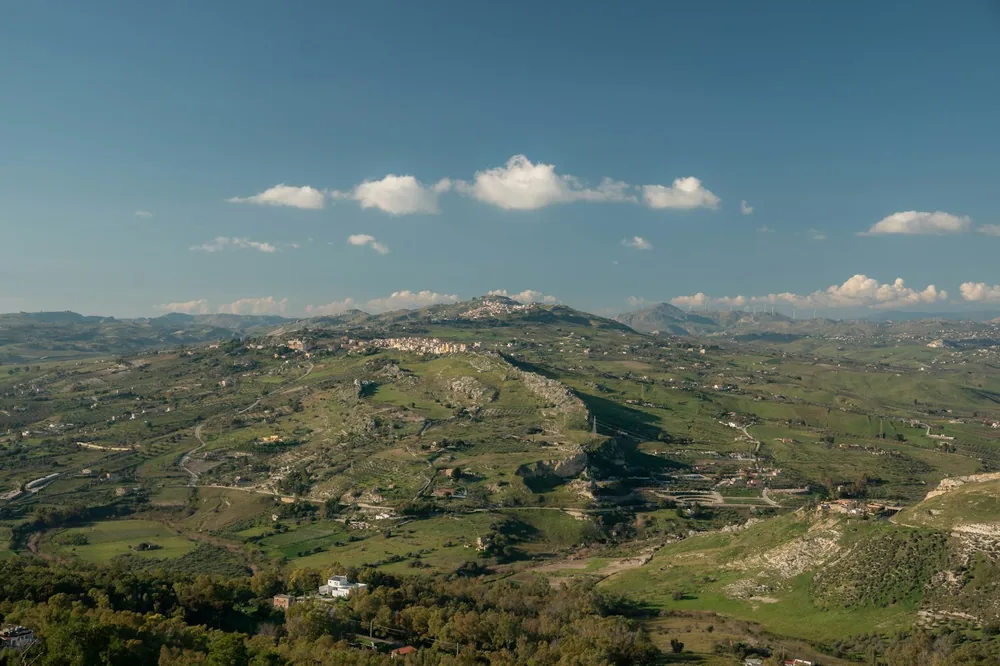 A vast green landscape with rolling hills and a town