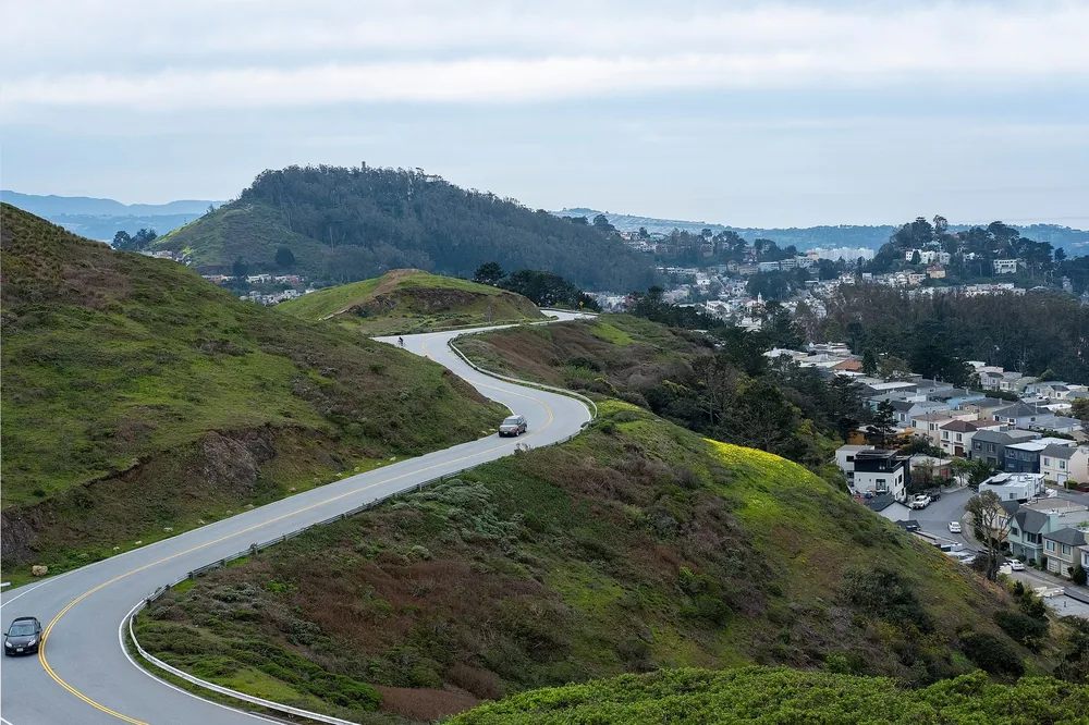 A winding road through lush green hills near a suburban town, ideal for travel inspiration