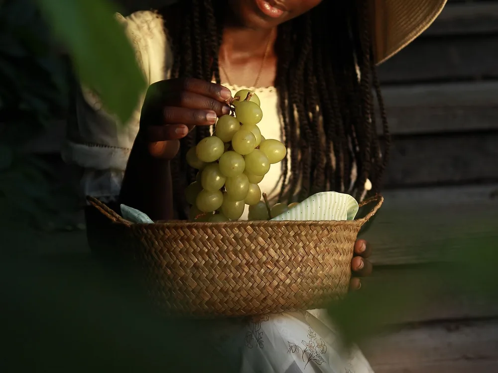 A woman enjoying a sunny day, holding a cluster of green grapes in a woven basket