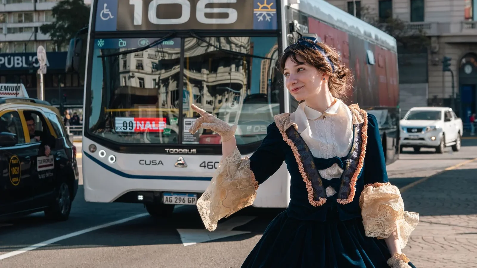 A woman in a vintage dress stands in front of a city bus on a busy street