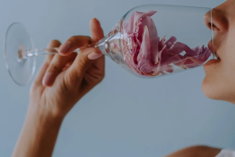 A woman's hand holding a wine glass containing a pink flower, creating an artistic and elegant visual