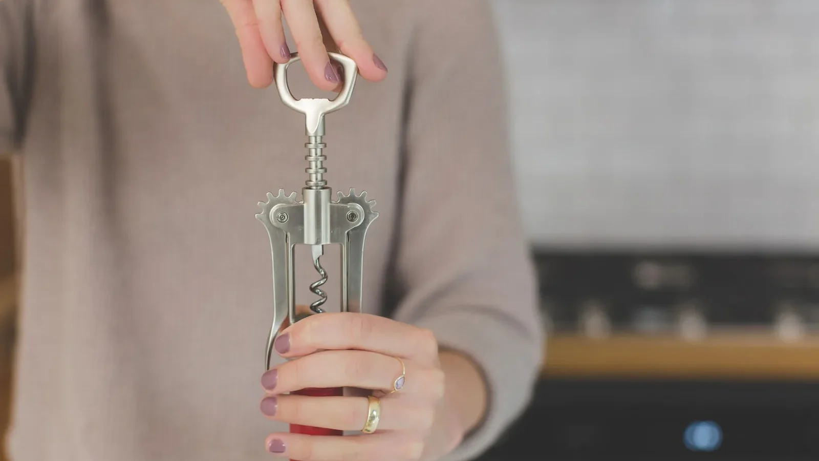 A woman using a corkscrew to open a wine bottle indoors