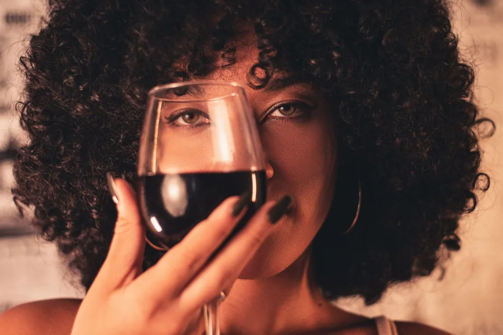 A woman with curly hair enjoys a glass of red wine, exuding elegance and celebration