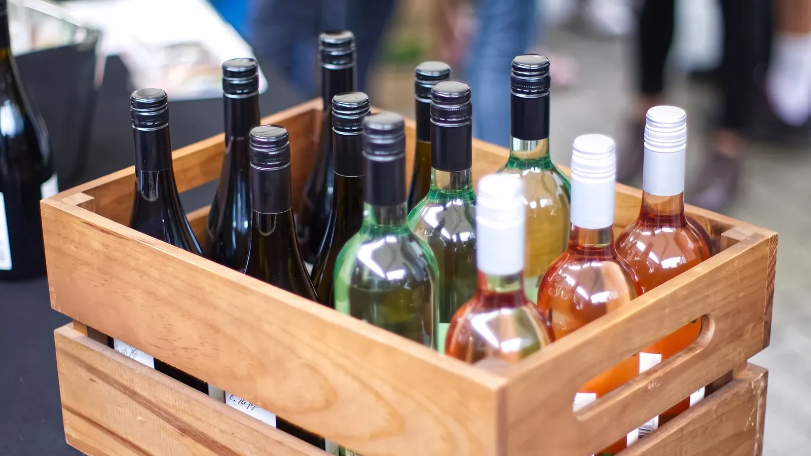 A wooden crate filled with diverse wine bottles at an outdoor gathering