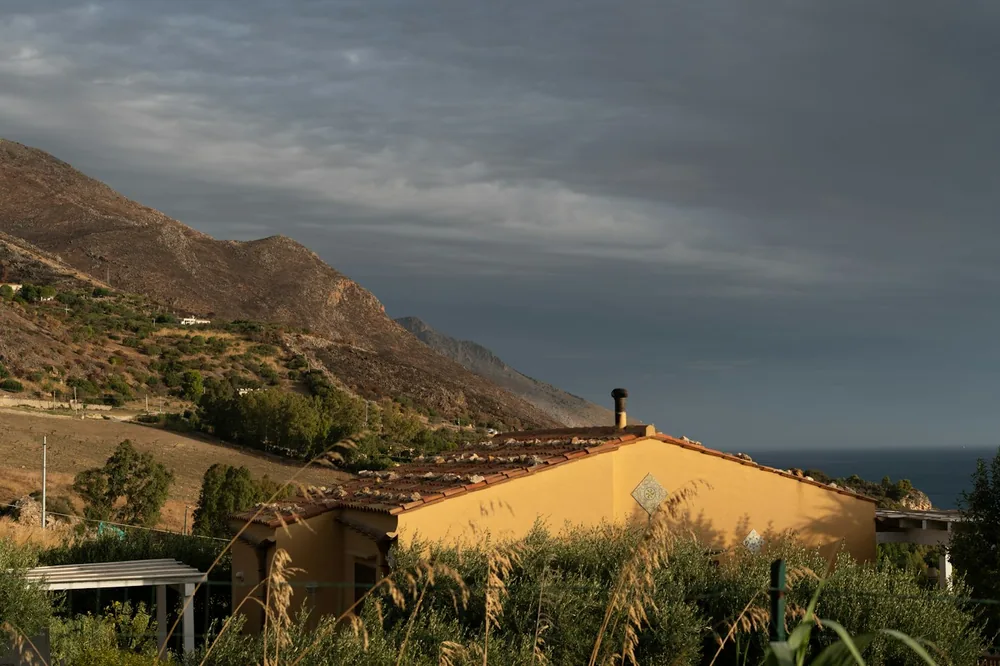A yellow house sits on a hill overlooking the ocean