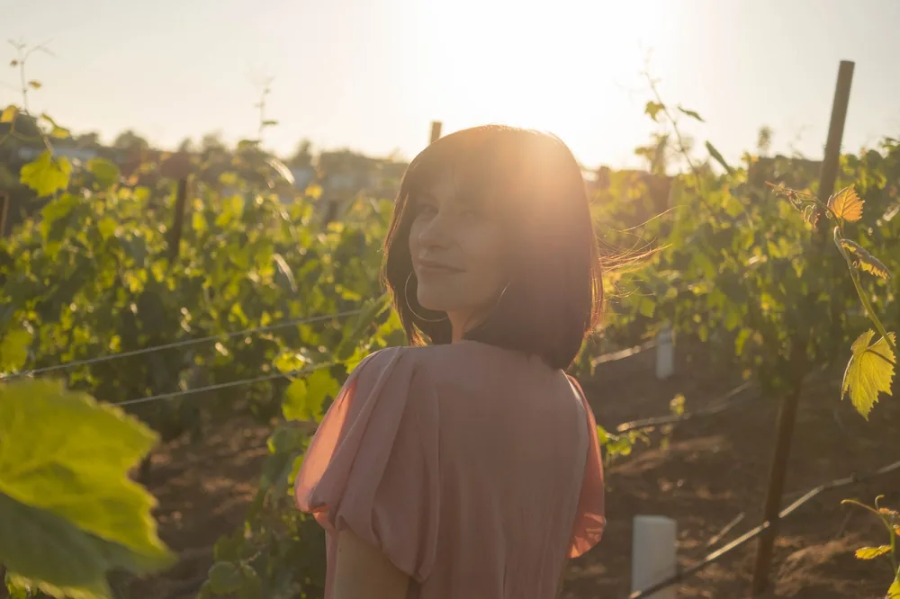 A young woman in a vineyard at sunset, backlit with a warm, glowing atmosphere