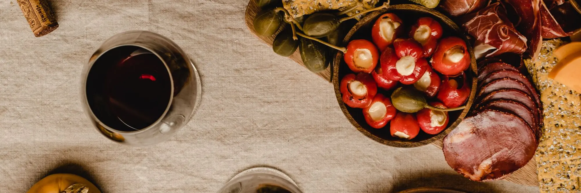 A glass of red wine beside a board of cured meats, cheese and olives on a linen cloth