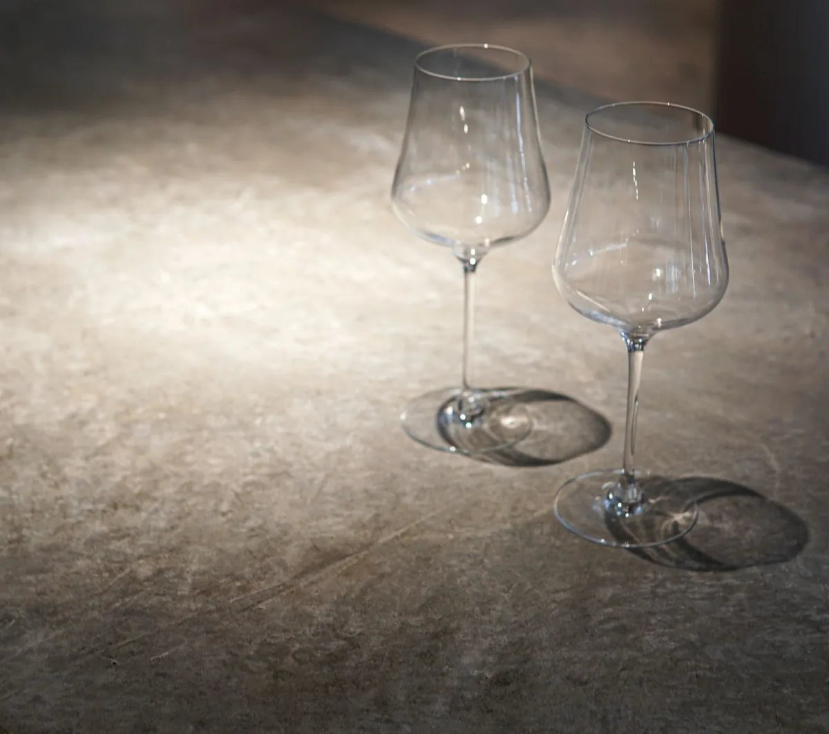 Two empty wine glasses casting shadows on a textured stone surface, suitable for dining themes