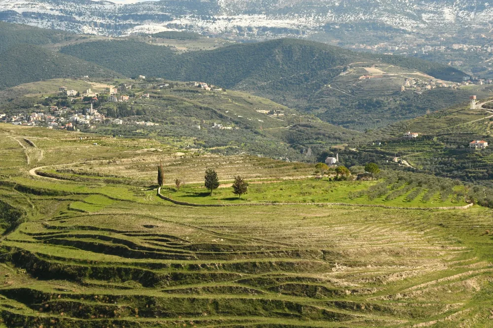 Aerial shot of terraced fields leading to a distant village nestled in verdant hills