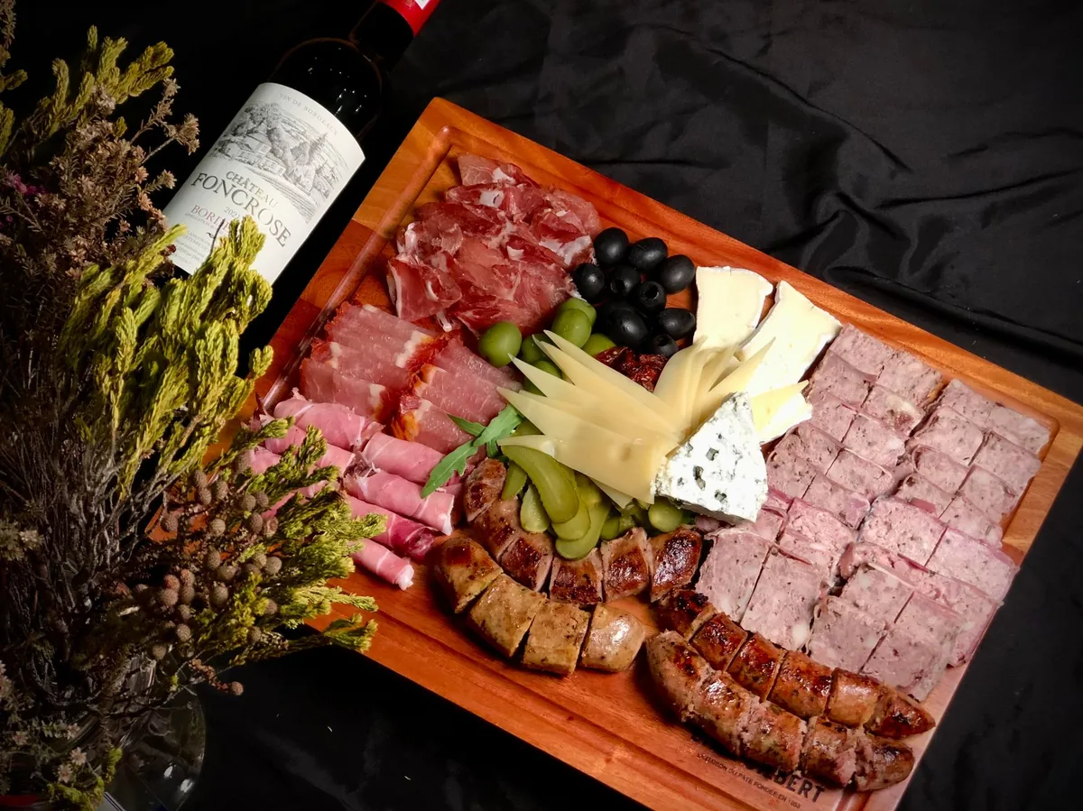 A board of cured meats and hard cheese beside a glass of dark red wine