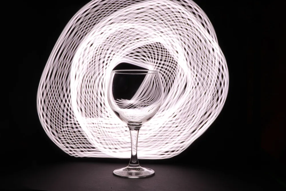 An artistic light painting featuring a wine glass against a spiral pattern background