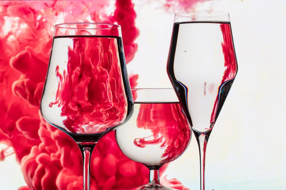 An artistic photo featuring wine glasses with red ink swirling in water, creating a vivid, abstract effect