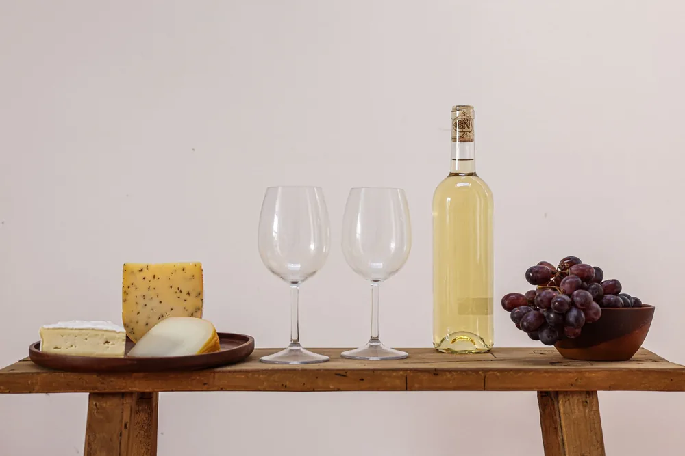 An elegant setup with white wine, cheese, and grapes on a rustic table