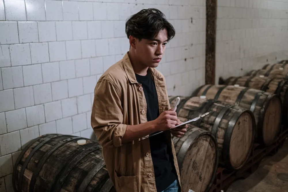 An expert brewer inspecting wooden barrels for craft beer fermentation in a brewery cellar