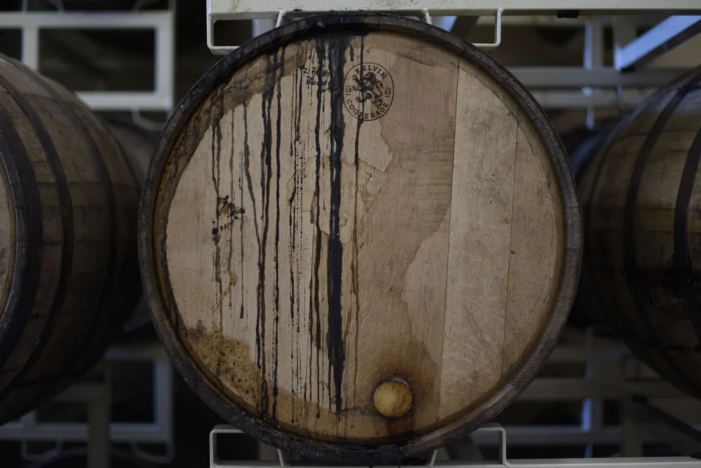 An oak barrel in a brewery cellar with dark liquid stains, ideal for themes of fermentation and distilling