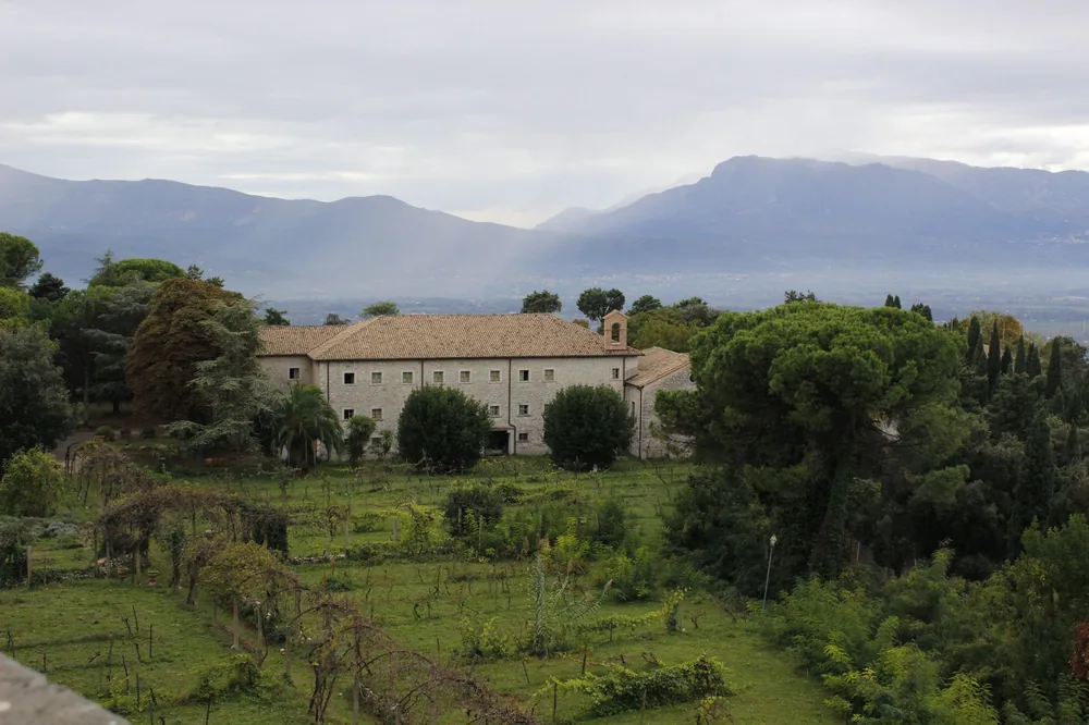 Ancient monastery amidst verdant countryside with mountains in the background, showcasing serene natural beauty