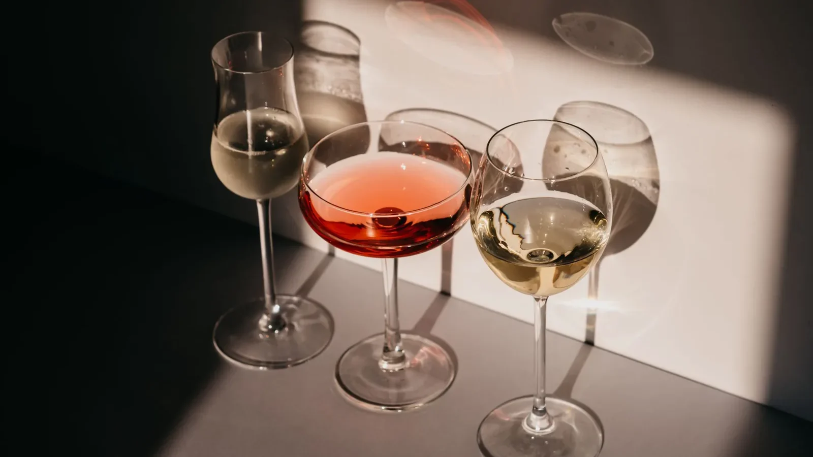 Arrangement of three wine glasses casting distinct shadows in warm light