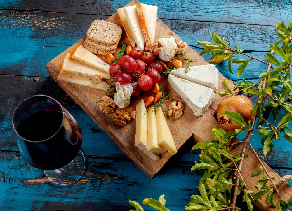 Artistic cheese board with red wine, nuts, and fruits on a blue table