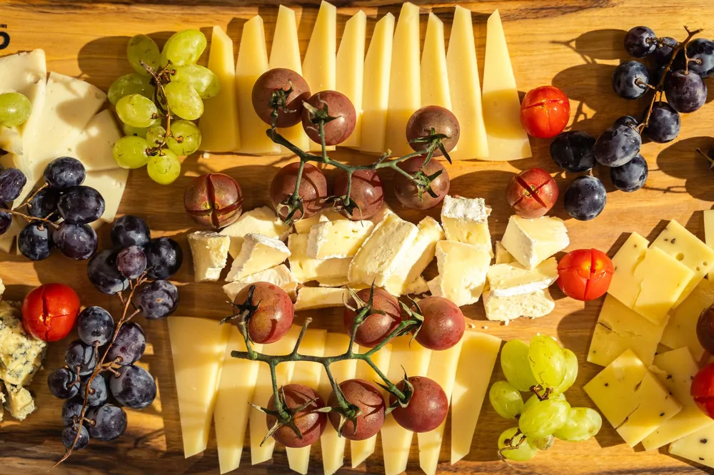 Assortment of cheese, grapes, and tomatoes on a wooden board, perfect for a gourmet appetizer