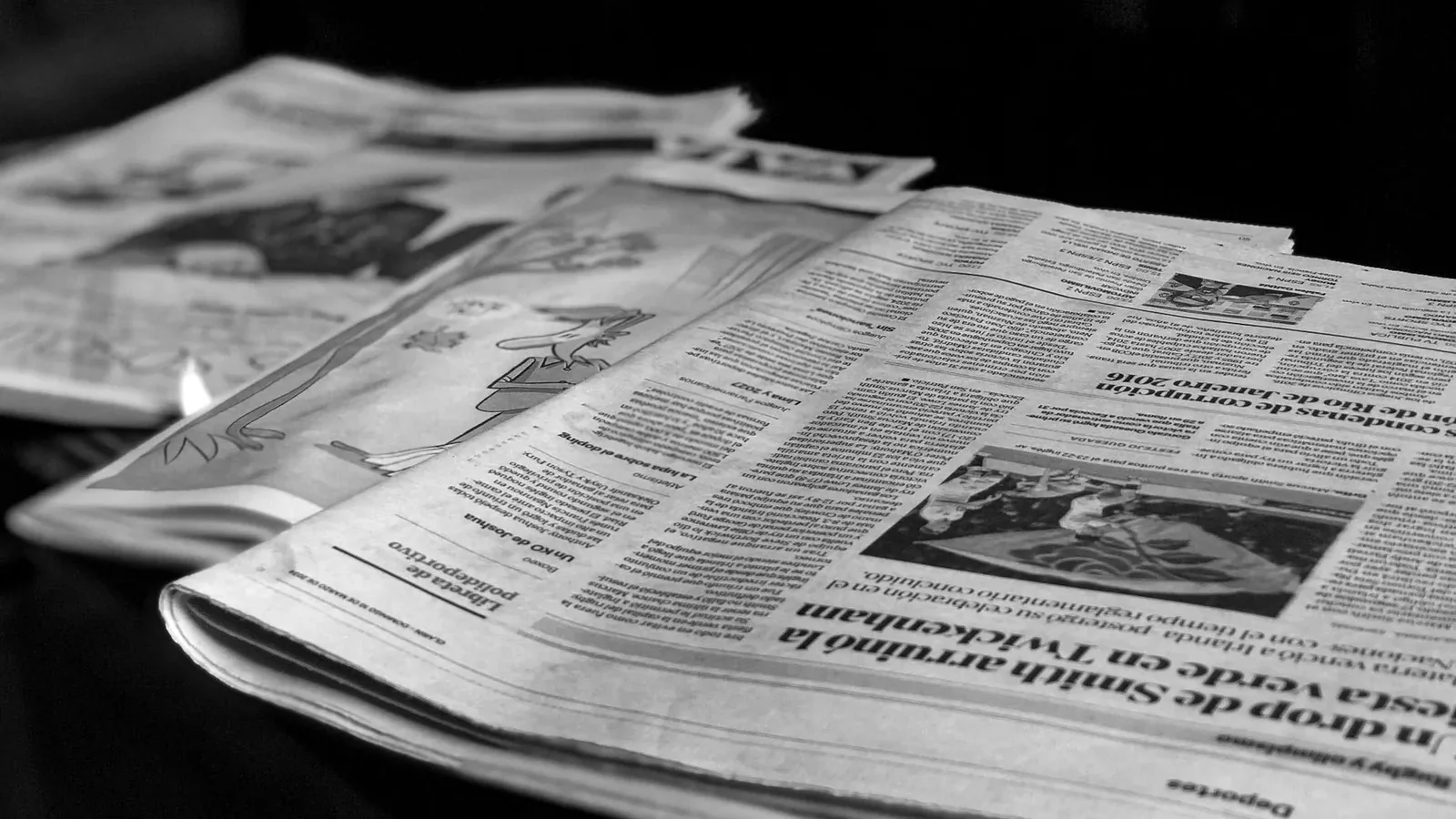 Black and white close-up image of newspapers laid on a table, emphasizing print media