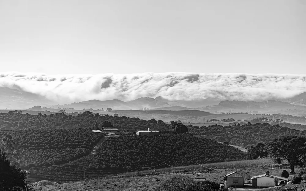 Black and white landscape with rolling clouds over mountainous terrain and farmland