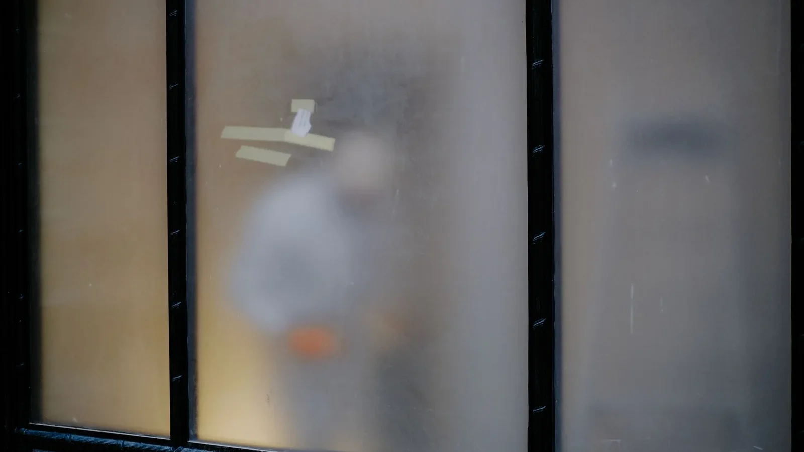 Blurry silhouette of a person seen through frosted glass with taped sections and black framing