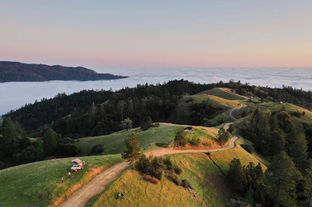 Car and people on green hill in sunset in summer time
