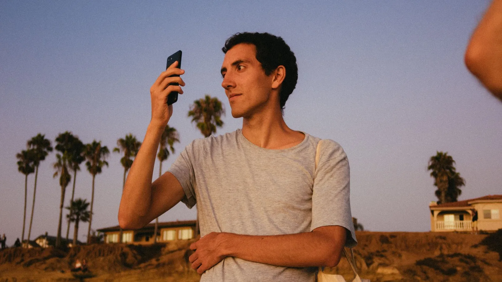 Casual man holding smartphone during sunset with palm trees in the background