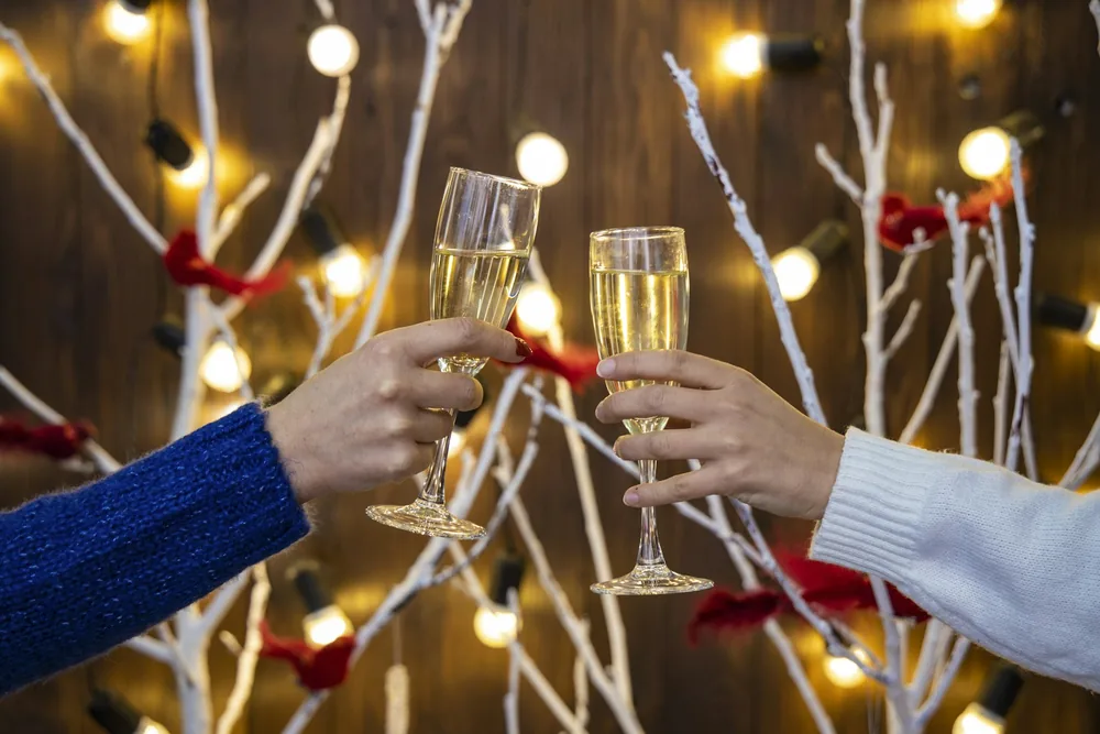 Champagne glasses in women hands on Christmas lights festive room decorated background indoor view holidays eve time