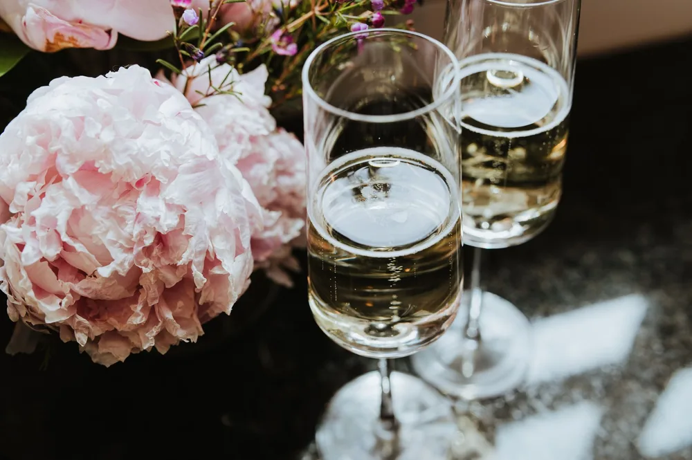 Champagne glasses on a table beside delicate pink peonies, creating an elegant setting