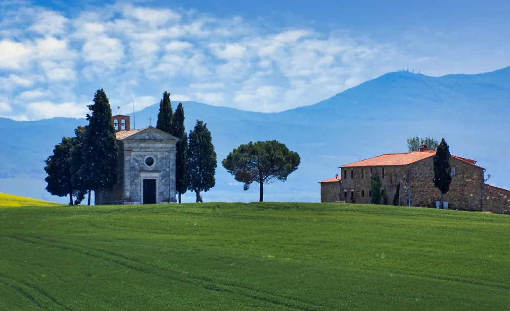Chapel and farmhouse on a lush green hill under a blue sky