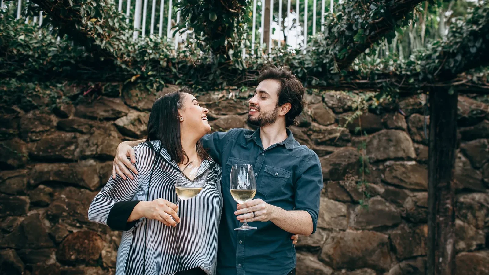 Cheerful couple enjoying wine outdoors against a rustic stone wall, exuding warmth and connection