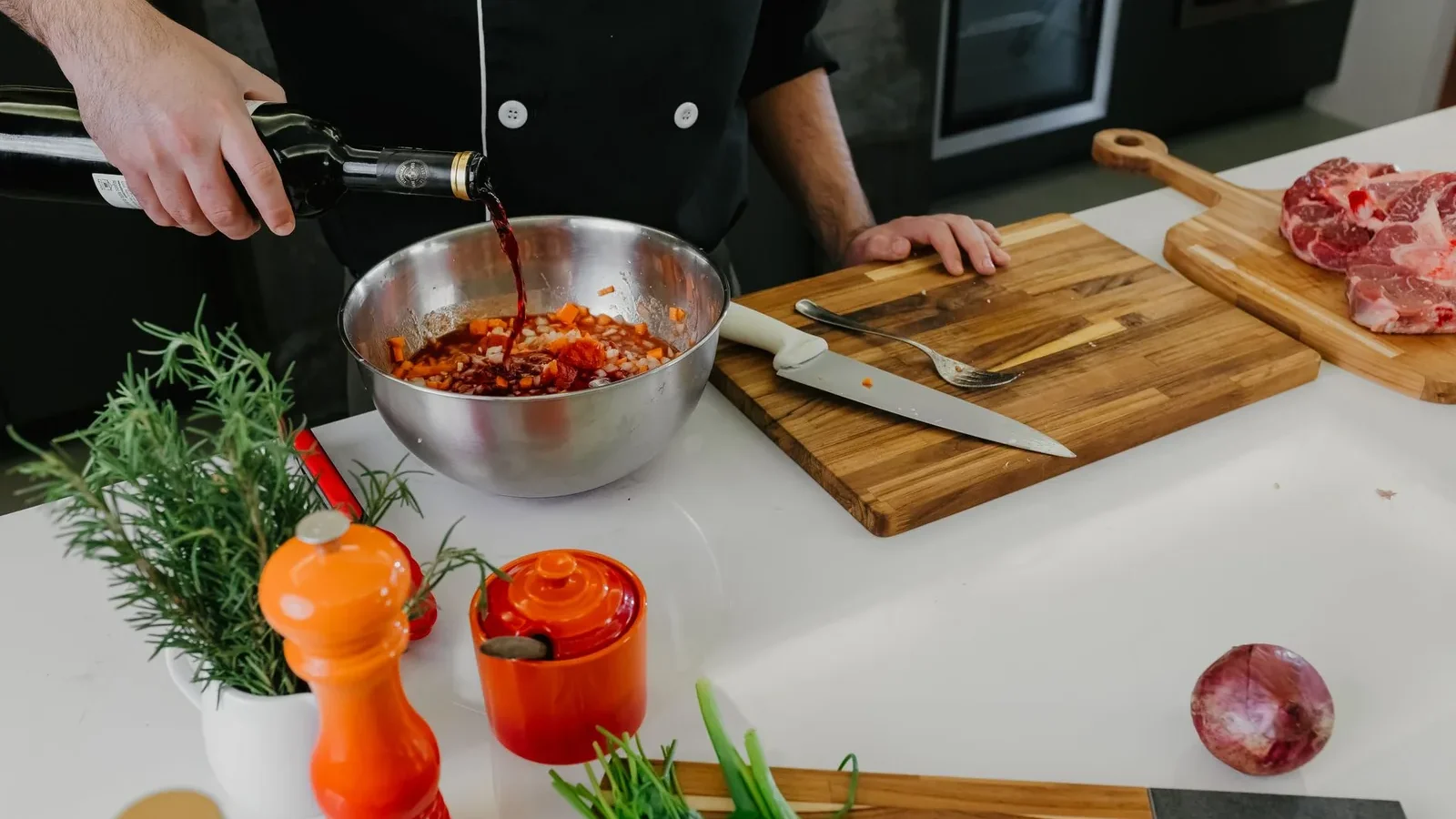Chef pouring red wine into bowl with herbs and spices for marinade preparation