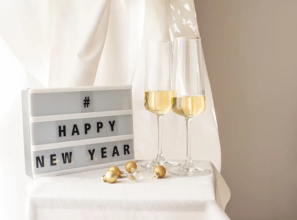 Chic New Year setup with champagne glasses and 'Happy New Year' sign on a white table