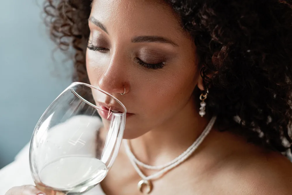 Close-up portrait of a black woman savoring a glass of white wine, eyes closed, exuding grace and beauty