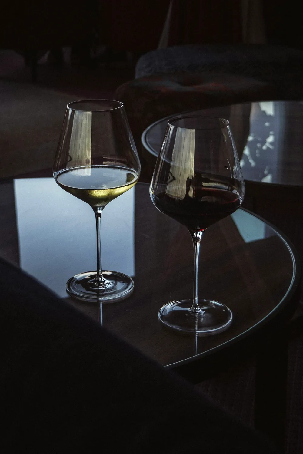 A glass of white wine and a glass of red wine side by side on a dark table