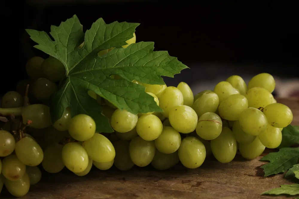 Cluster of ripe green grapes with a leaf on a wooden surface. Perfect for culinary visuals