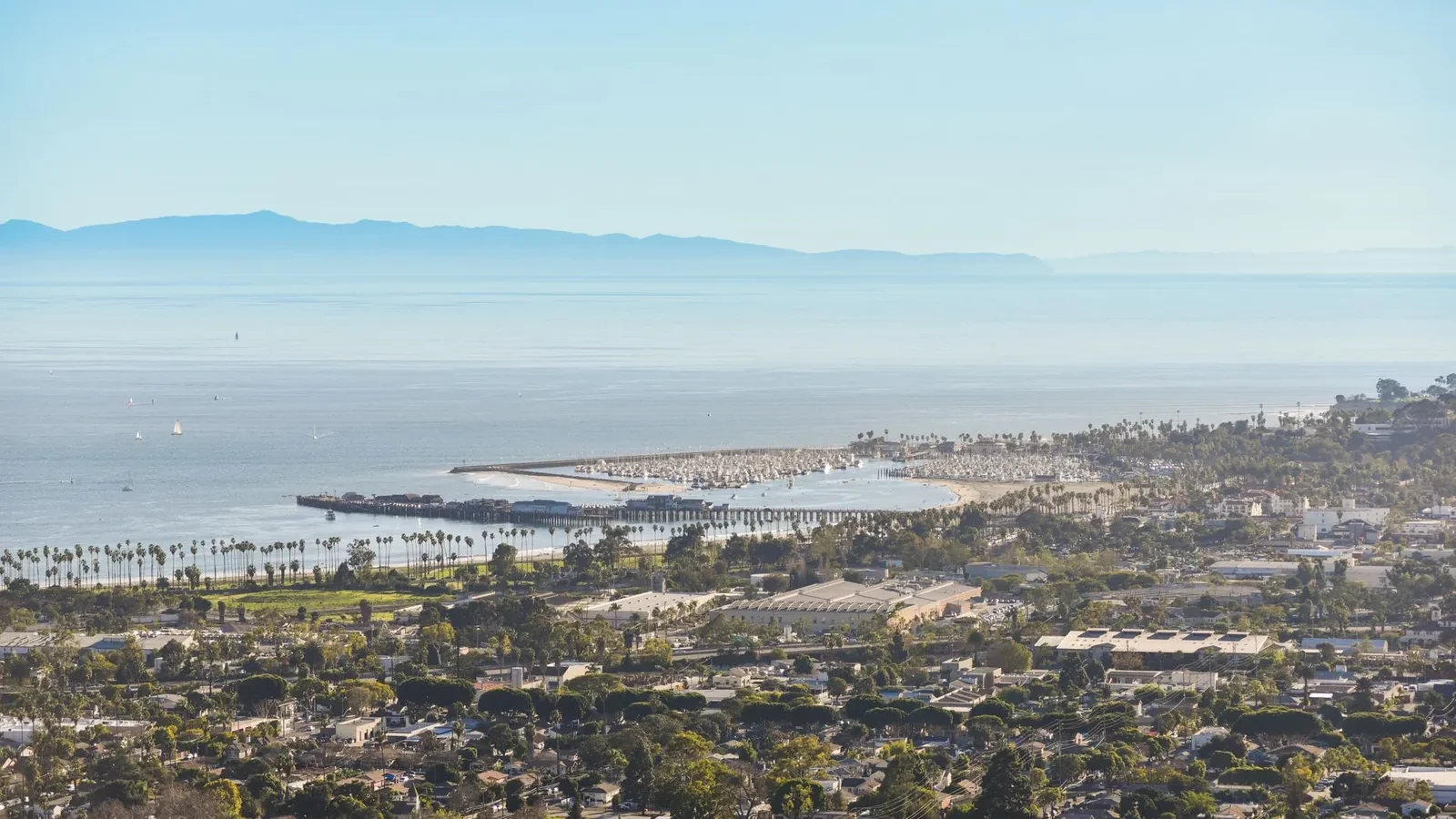 Coastal city with ocean, beach, and mountains under a bright blue sky