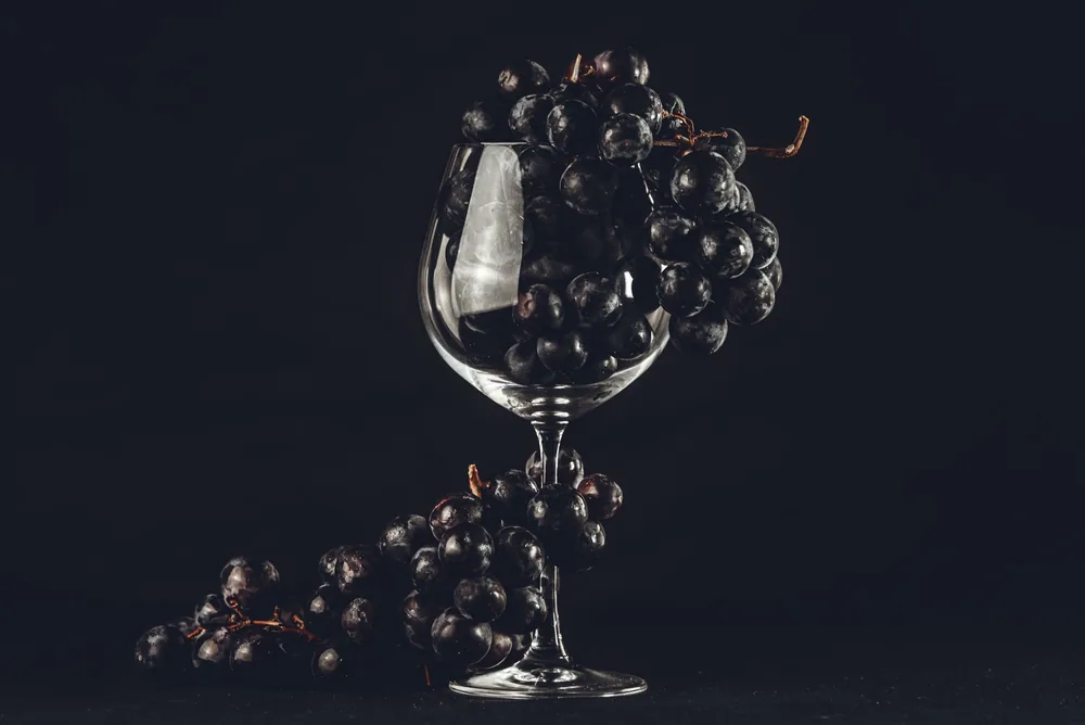 Composition featuring black grapes artfully arranged in a wine glass