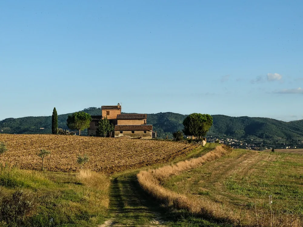 Countryside landscape with fields, farmhouse, and hills under a clear blue sky