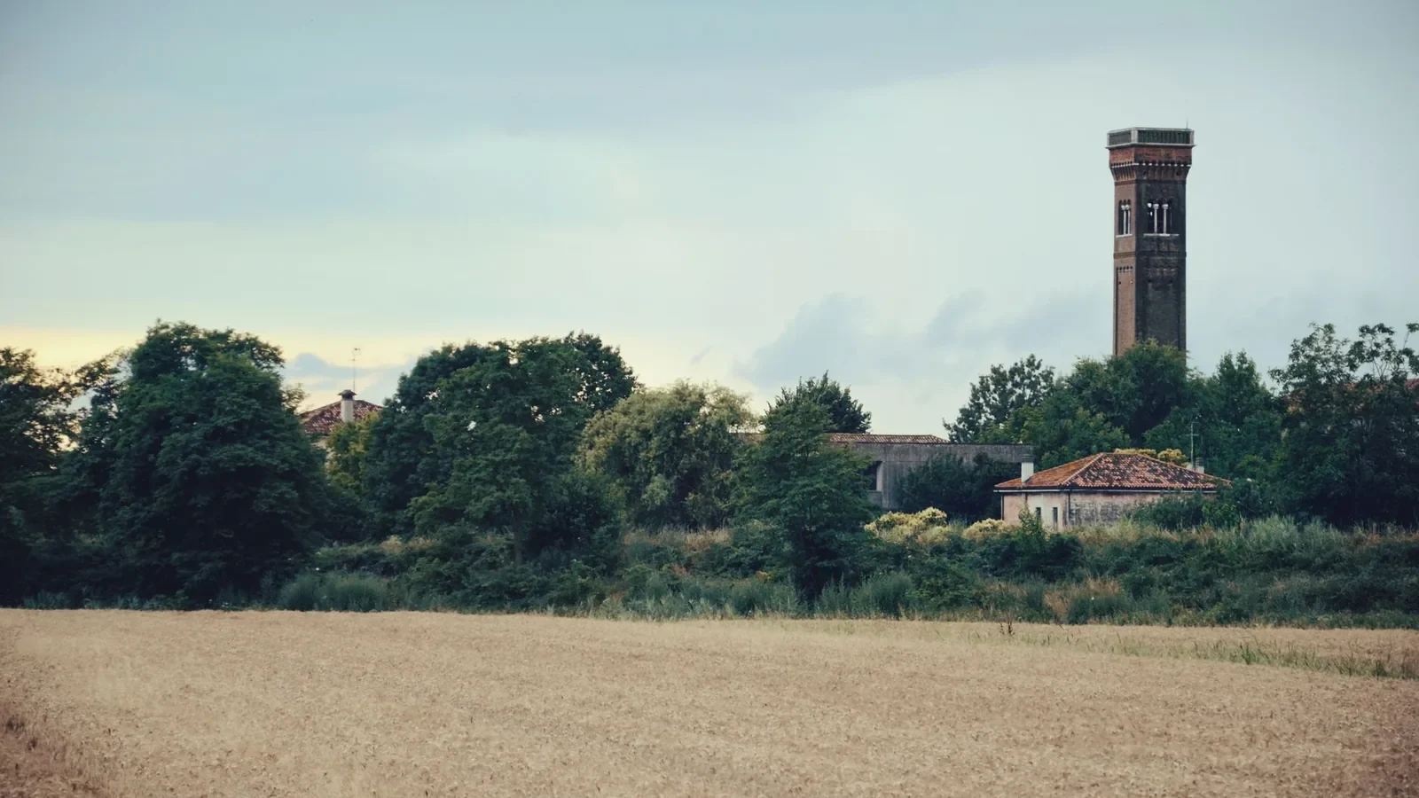 Countryside view featuring a distant rustic tower and expansive fields under a cloudy sky