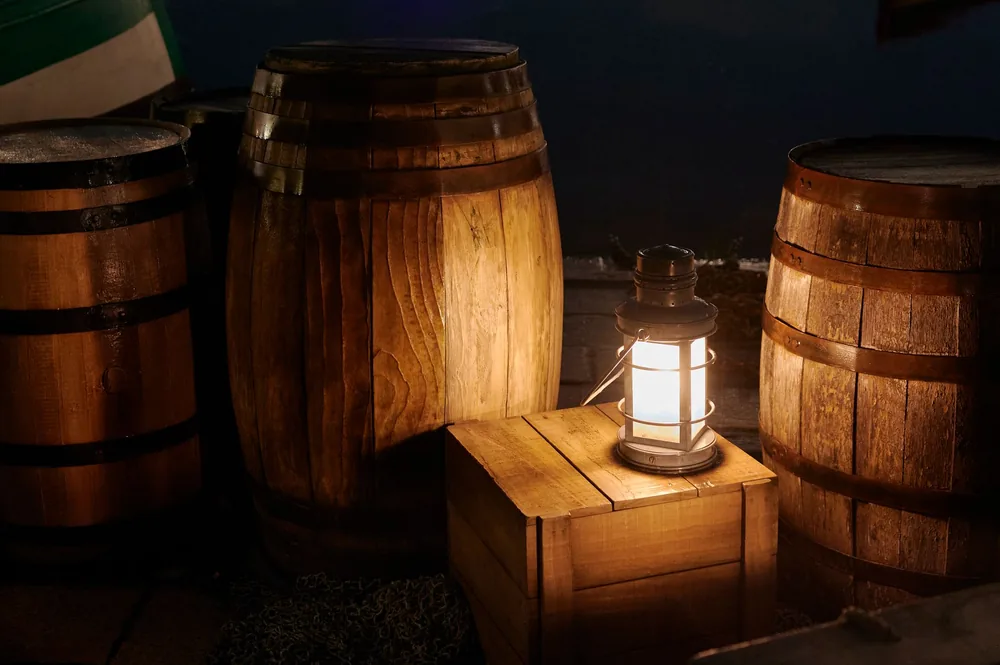 Cozy scene of wooden barrels and lantern casting warm light in a rustic outdoor setting at night