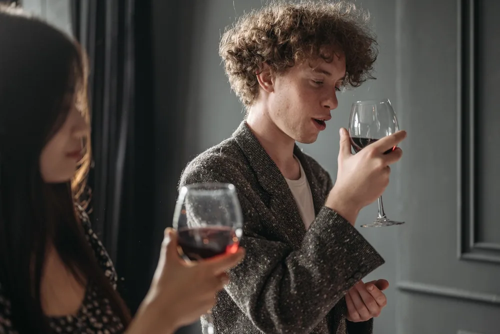 Curly-haired man and woman with glasses enjoying red wine indoors